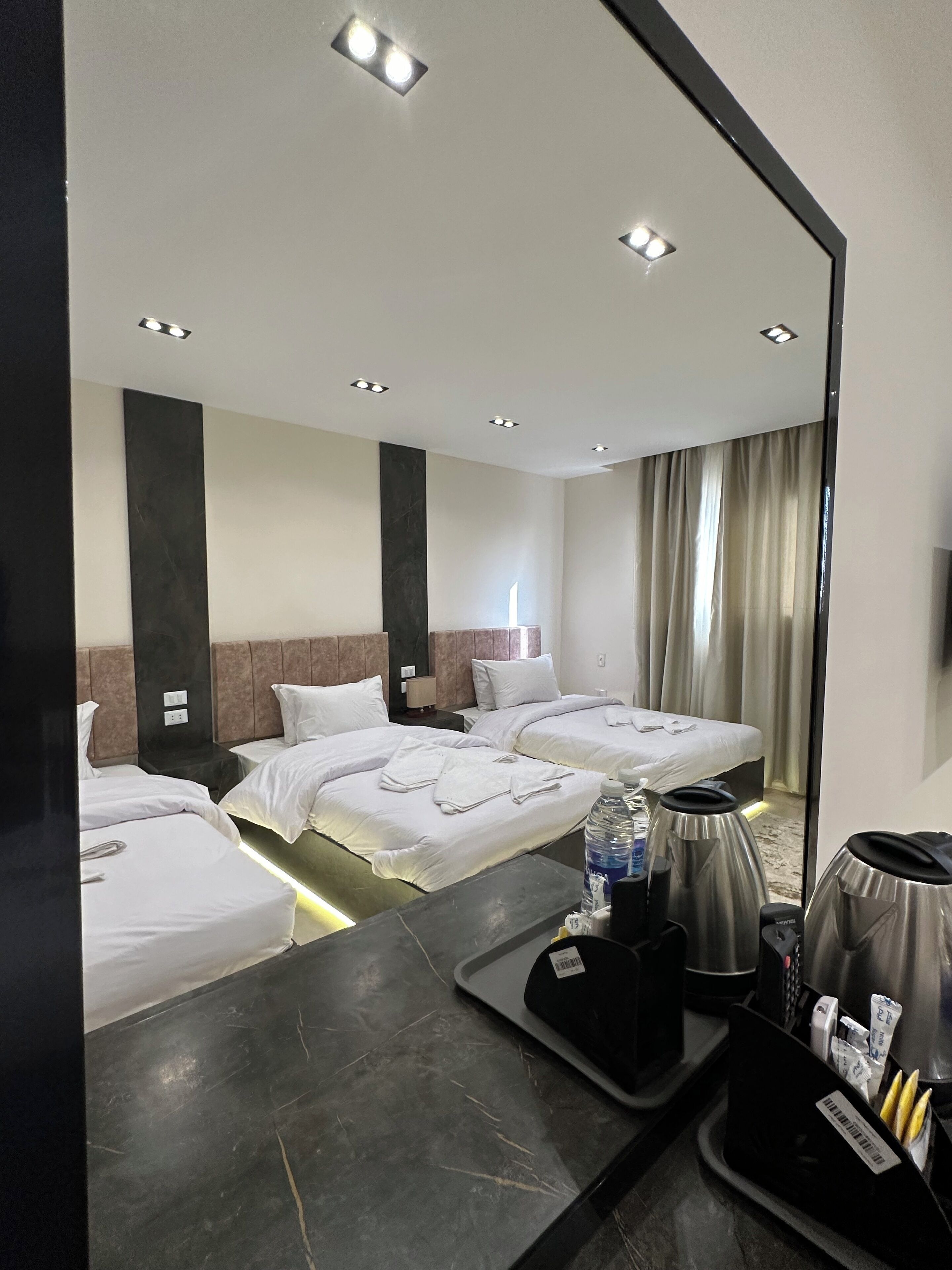 A hotel room with two beds, a large mirror, a coffee maker, and a tray with toiletries.