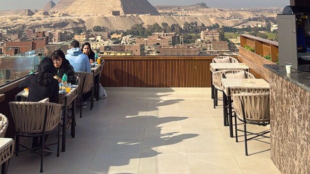 Terraza en la azotea con mesas y sillas, ofreciendo vistas a las pirámides en la distancia.