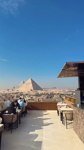 Une terrasse sur le toit, aménagée avec des tables et des chaises, d’où l’on peut admirer les pyramides au loin.