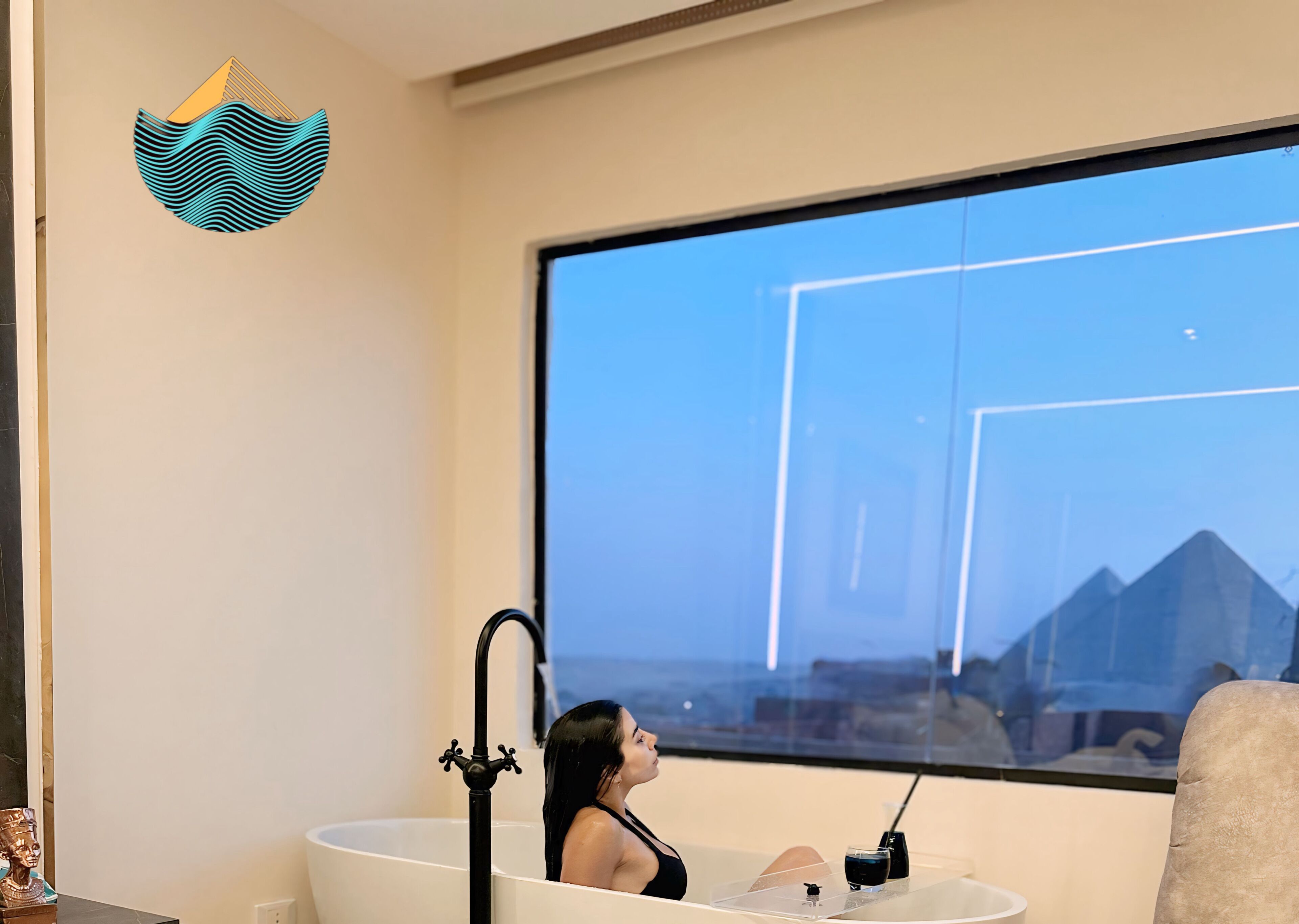 A person in a bathtub with a view of pyramids through a large window.