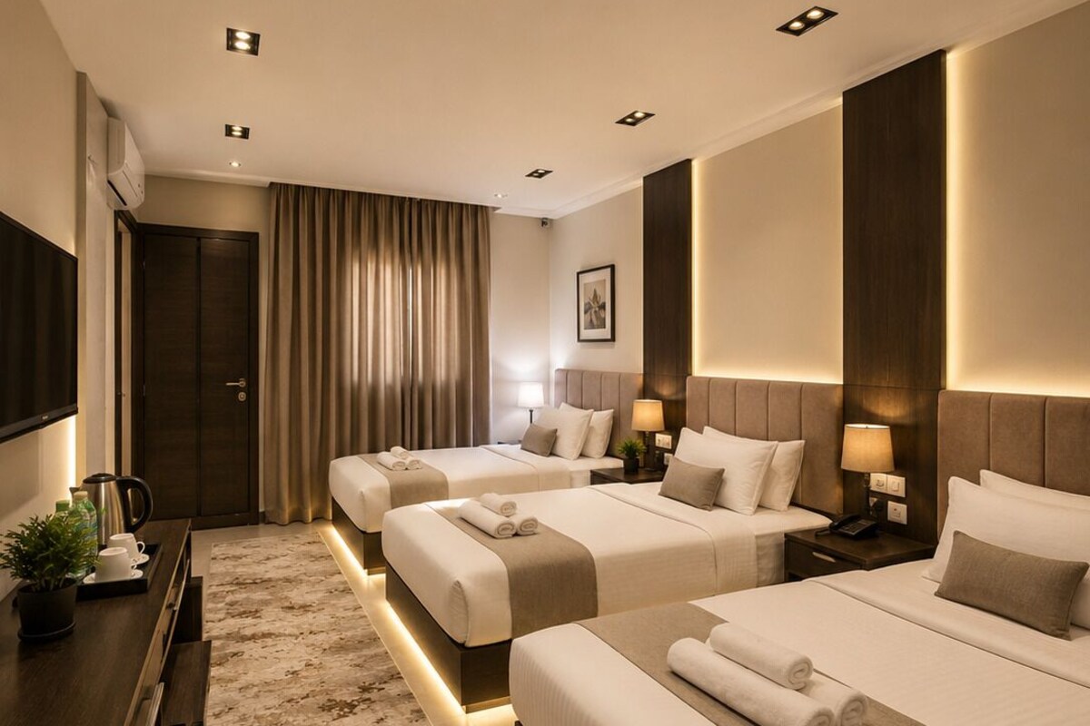 A hotel room with three beds, a desk with a coffee maker, and a TV.