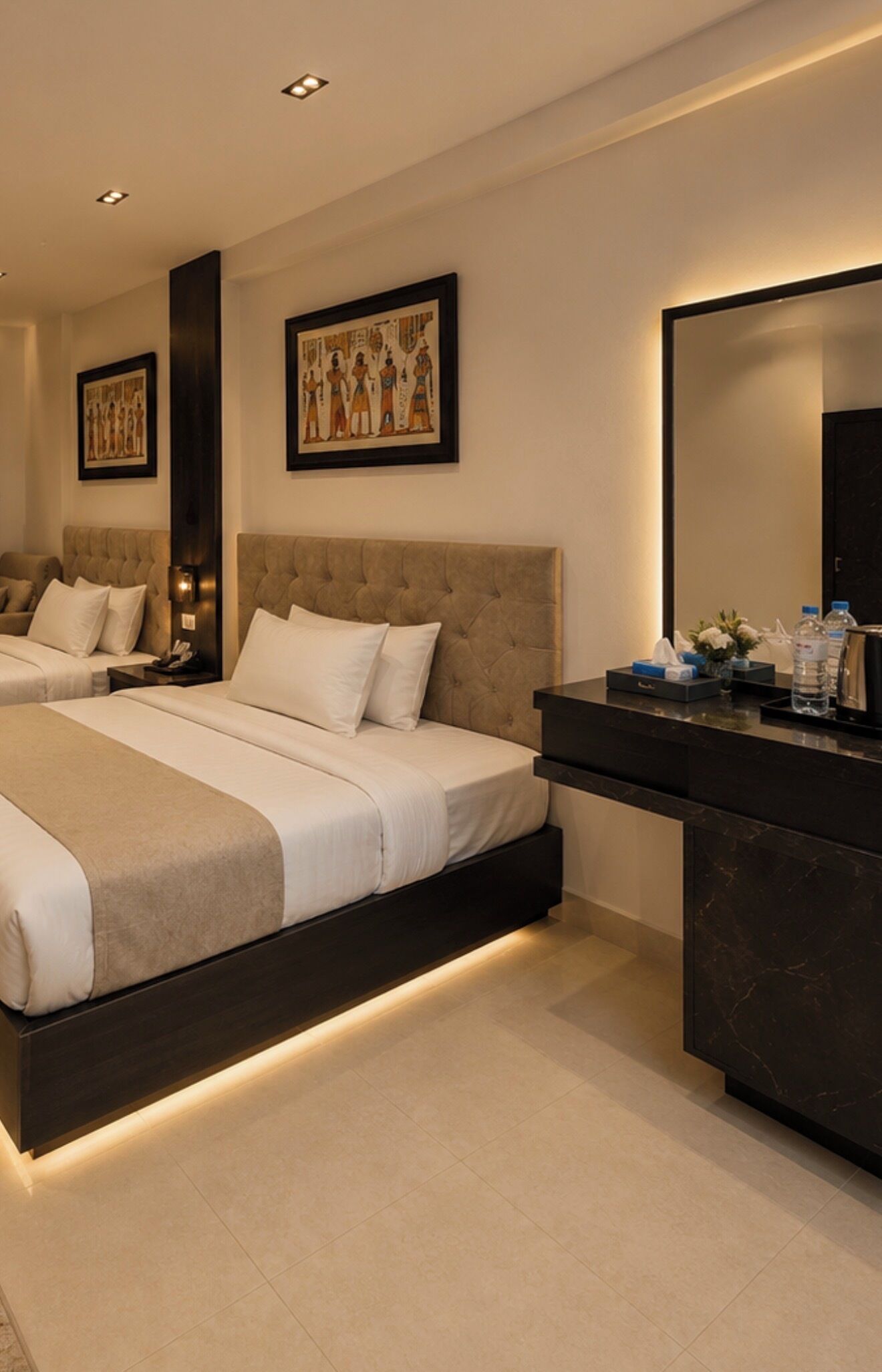 A modern hotel room with two beds, a dark-toned vanity, and artwork on the walls.