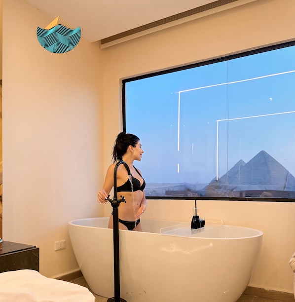 Une femme se tient dans une baignoire, et par la fenêtre, on aperçoit des pyramides.