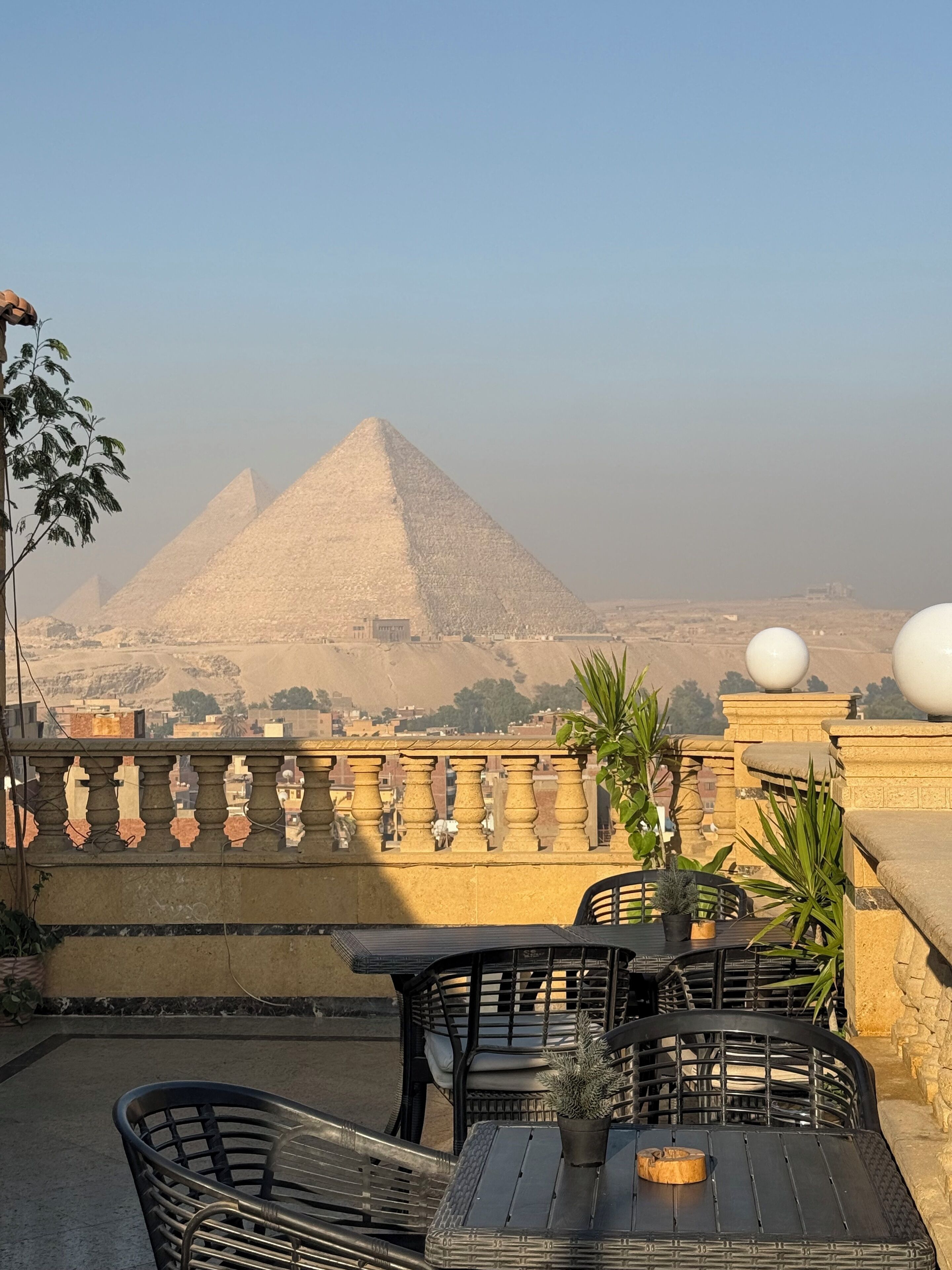 A terrace with outdoor seating, a view of the pyramids, and a stone balustrade.