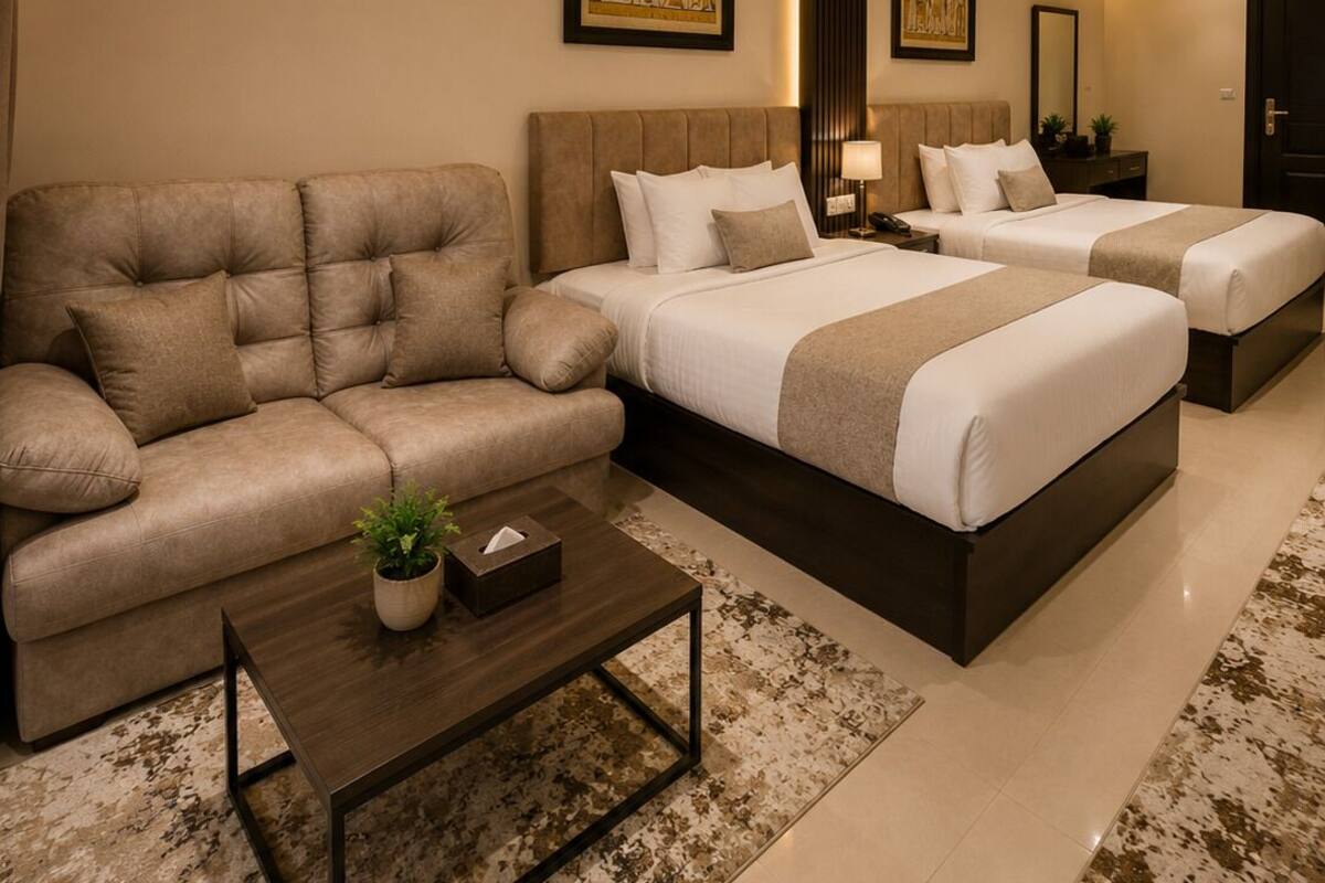 A modern hotel room with a sofa, two beds, a coffee table, and artwork on the walls.