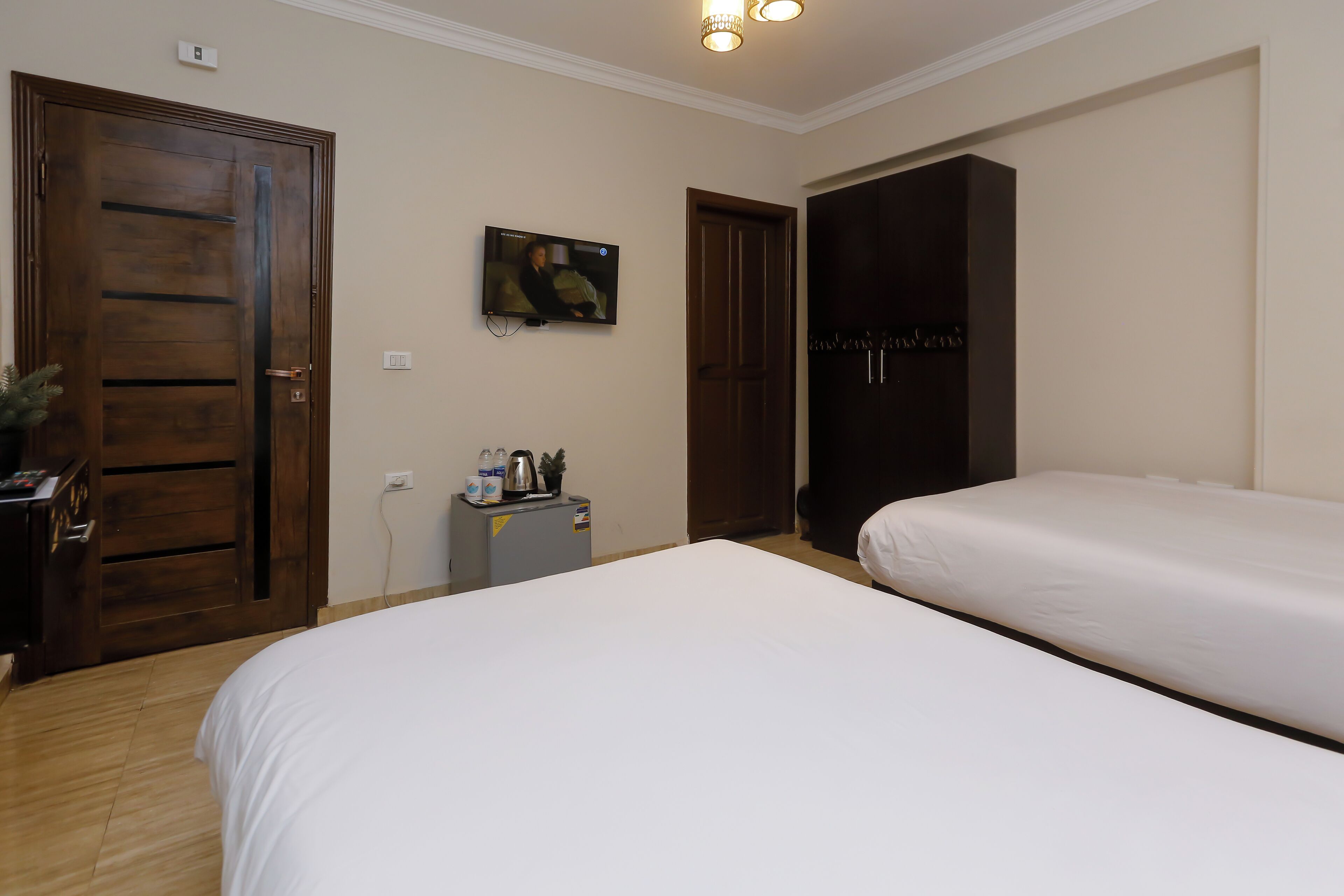 A hotel room with two beds, a TV, a wardrobe, and a small desk with a kettle and cups.