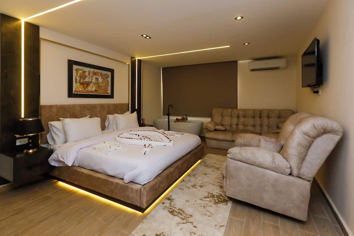 A modern bedroom with a large bed, a sofa, a bedside table, and a wall-mounted TV.