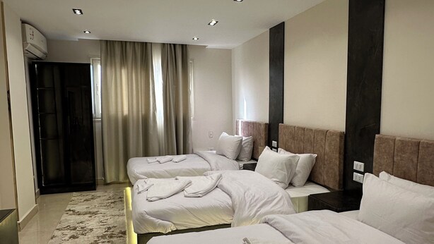 A hotel room with two beds, a large window with curtains, a modern headboard, and a marble floor. - Crowne pyramids palace (Giza)