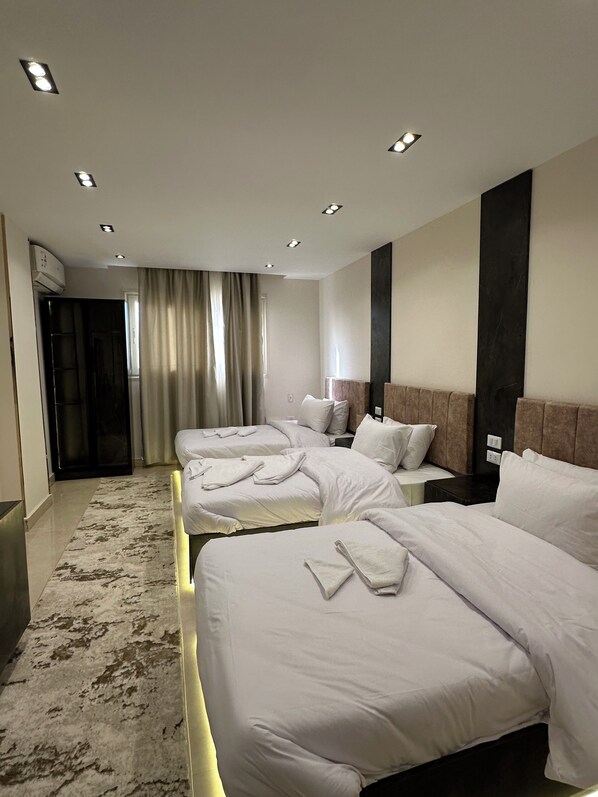 A hotel room with two beds, a large window with curtains, a modern headboard, and a marble floor.