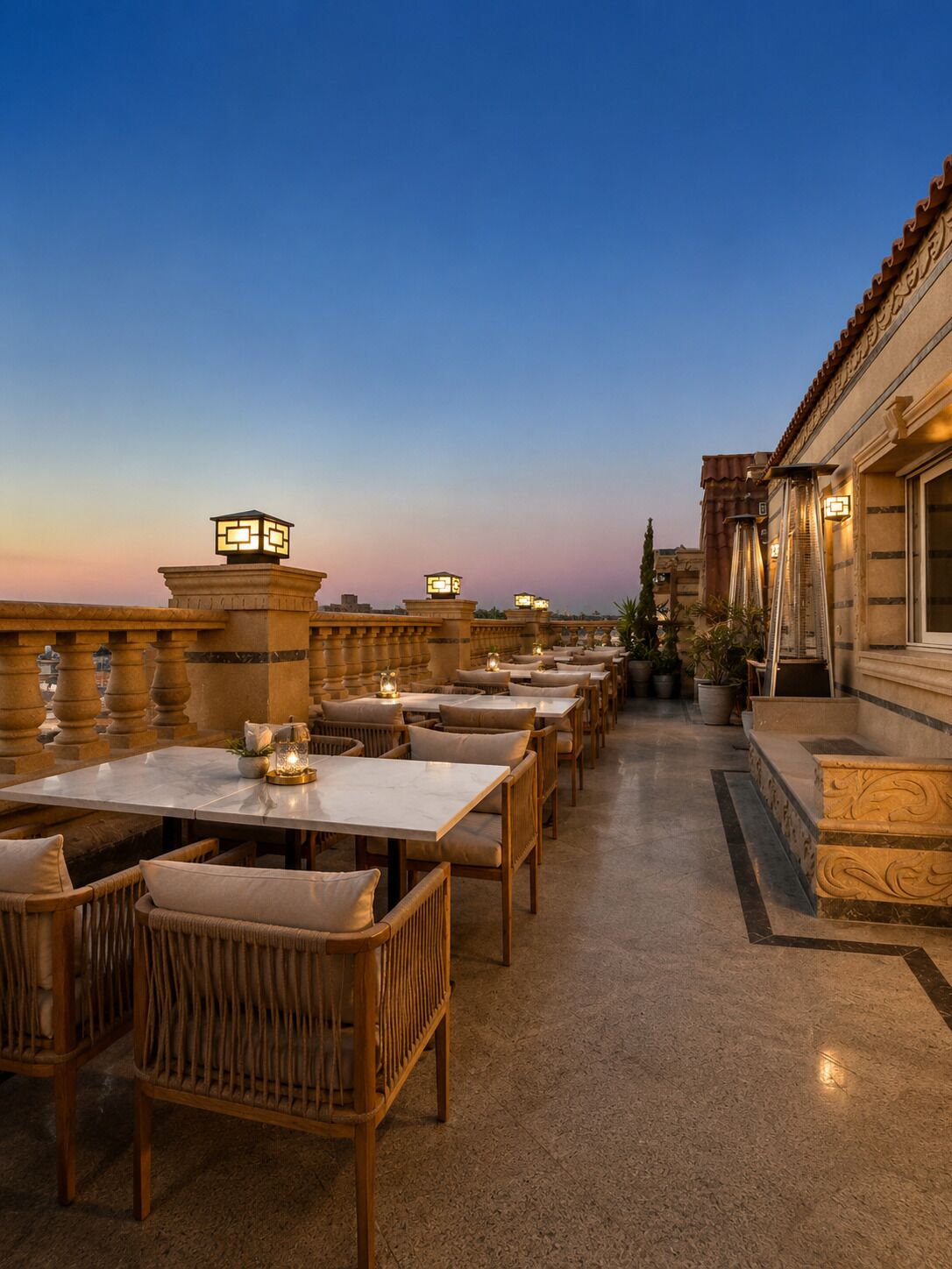 An outdoor dining area with tables and chairs, a stone balustrade, and a building with a tiled roof.