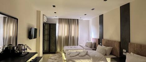A hotel room with three beds, a desk with a flat-screen TV, and a large window with curtains.