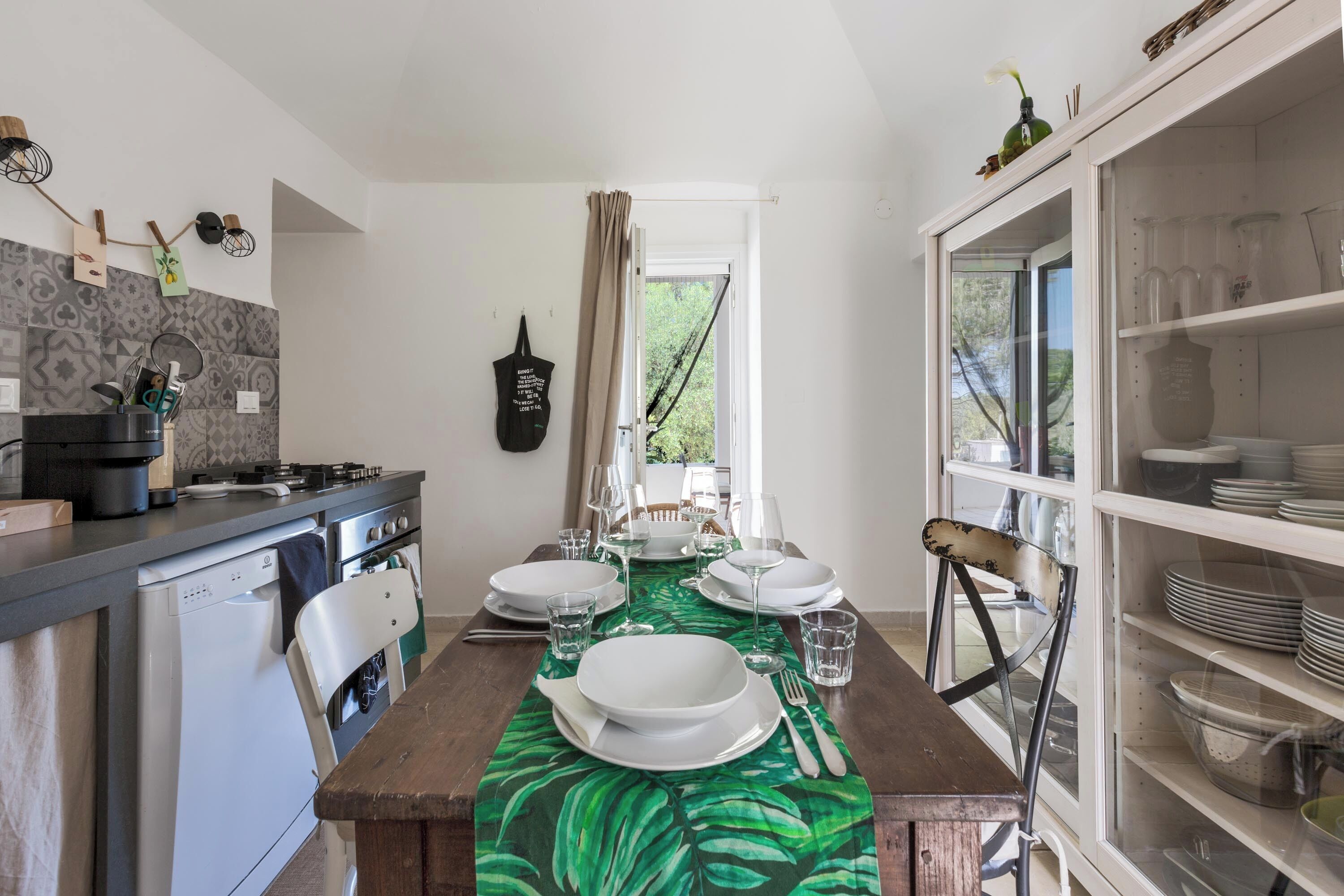 Une cuisine avec une table à manger dressée pour six personnes, un réfrigérateur blanc et un meuble contenant de la vaisselle.