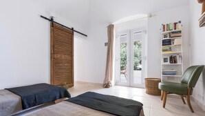 Une chambre avec deux lits, une bibliothèque, une chaise et une porte coulissante donnant sur un balcon.