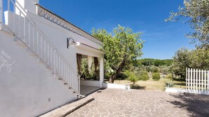 Un bâtiment blanc avec une entrée pavée de pierres, une clôture blanche et un arbre en arrière-plan.