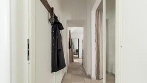 Un couloir étroit aux murs blancs, un manteau accroché sur le côté gauche et une porte au fond.