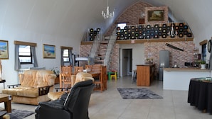 A spacious living area with a high ceiling, a staircase to an upper level, and a wall decorated with vinyl records. - Arch Cabins Self Catering (Storms River)