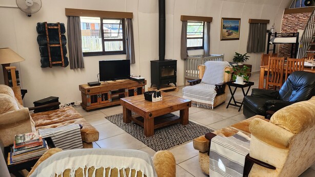 A cozy living room with a TV, fireplace, comfortable seating, and a bookshelf. - Arch Cabins Self Catering (Storms River)