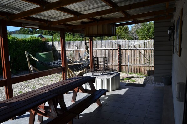 A covered patio area with a wooden bench, a hammock, and a table.