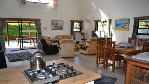 A spacious living area with a kitchen, dining table, and comfortable seating. - Arch Cabins Self Catering (Storms River)