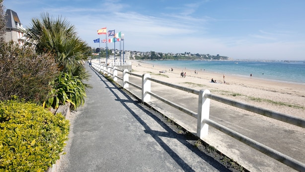 A coastal walkway with a concrete railing, palm trees, and flags. - l'Emérillon - Appt à 200m de la plage (Saint-Cast-le-Guildo)
