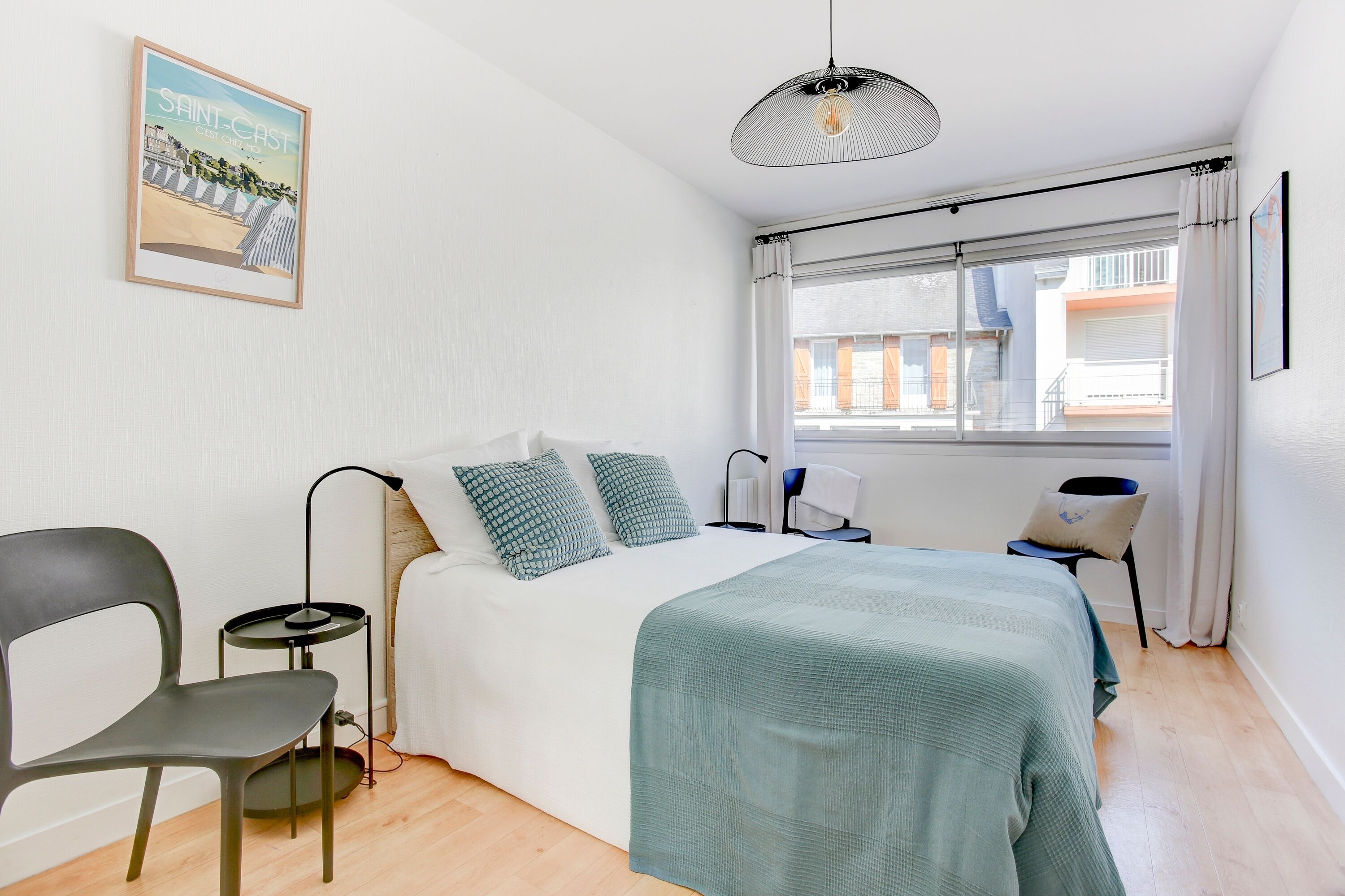 Una camera da letto moderna con un letto, una sedia, un comodino, una lampada e una finestra con tende.