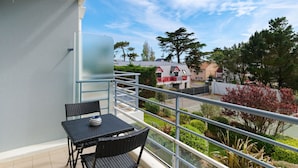 Varanda com mesa e cadeiras, vista para um jardim e um edifício com telhado vermelho.