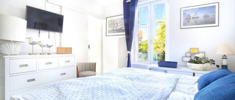 Un dormitorio con cama, televisión, cómoda, ventana con cortinas y vistas al exterior.