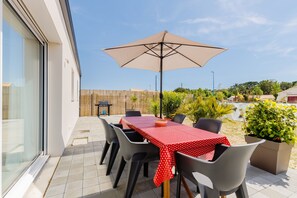 Eine Terrasse im Freien mit Tisch, Stühlen, einem großen Sonnenschirm und Topfpflanzen.