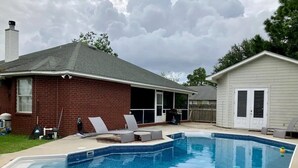 Un patio trasero con piscina, una casa de ladrillo y una casa blanca.
