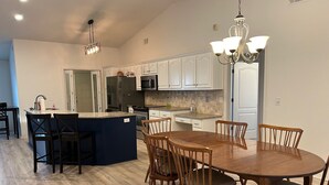 Una cocina moderna con armarios blancos, una isla central y un comedor con mesa y sillas de madera.