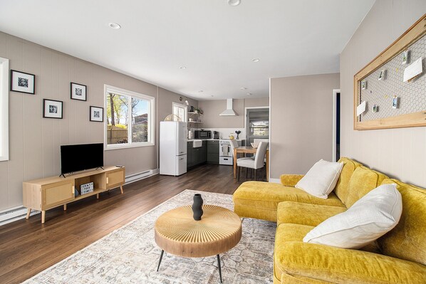 A modern living room with a yellow sofa, a wooden coffee table, and a flat-screen TV.