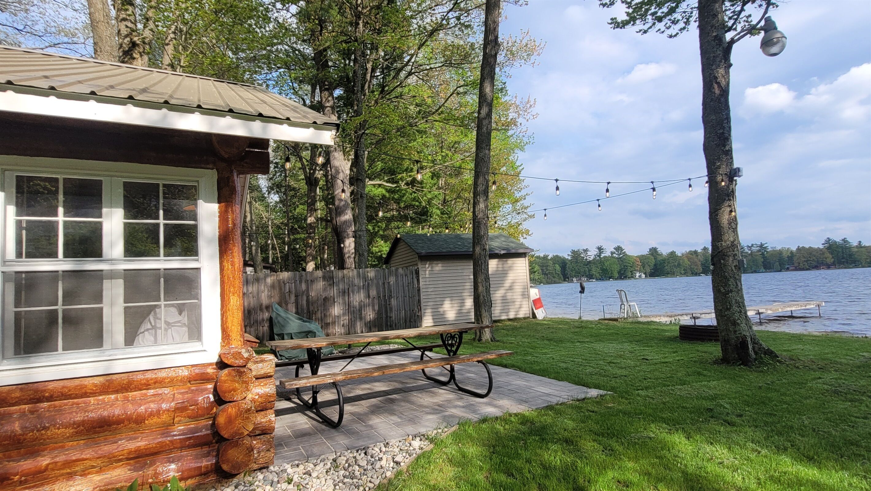 A cabin with a picnic table and a dock extending into a lake, surrounded by trees.
