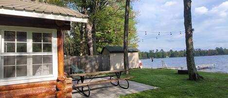 A cabin with a picnic table and a dock extending into a lake, surrounded by trees.