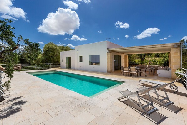 Une maison moderne dotée d’une piscine, d’un espace salon extérieur et d’un patio couvert.