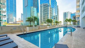 A swimming pool with lounge chairs, surrounded by high-rise buildings. - Curated Sky Abode: Ocean & City views, Sleeps 6 (Miami)