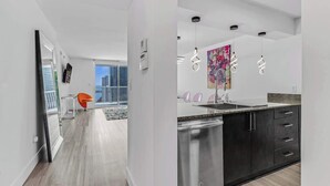 A modern kitchen with dark cabinets, a stainless steel dishwasher, and pendant lights. - Curated Sky Abode: Ocean & City views, Sleeps 6 (Miami)