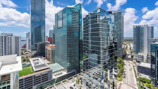 A high-rise urban area with modern glass buildings, a clear sky, and a road with vehicles. - Curated Sky Abode: Ocean & City views, Sleeps 6 (Miami)