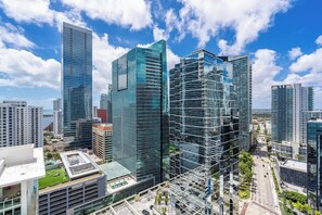 Zona urbana com edifícios altos de vidro modernos, céu claro e uma estrada com veículos.