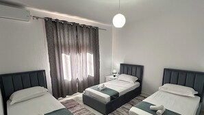 A modern hotel room with three single beds, a small table, a nightstand, and a large window with curtains. - Family - sized villa , pet friendly , city and castle view with a big garden ! (Berat)