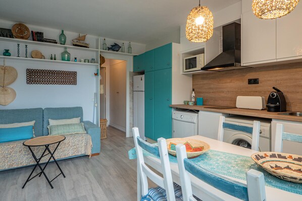 A compact kitchen with a microwave, toaster, and sink. There is a dining area with a table and chairs.