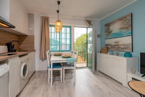 Een compacte keuken met een wasmachine, een eethoek met een tafel en stoelen, een televisie en een groot raam met uitzicht op groen.