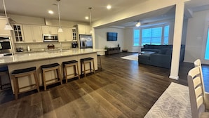 A modern kitchen with a central island, bar stools, and a dining area with a wooden table.