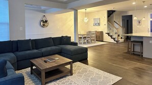A modern living room with a sectional sofa, a wooden coffee table, and a dining area with a chandelier.
