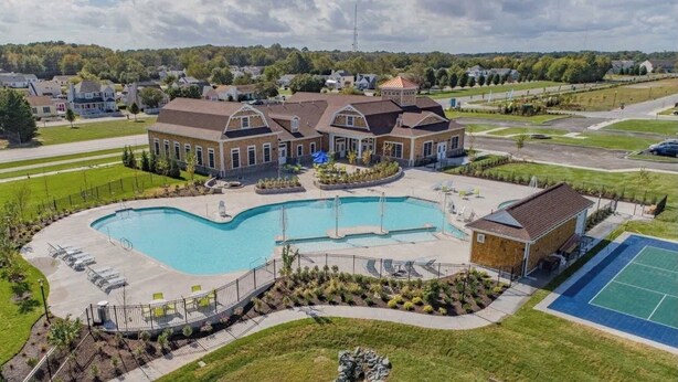 A residential area with a large swimming pool, a tennis court, and houses with brick exteriors.