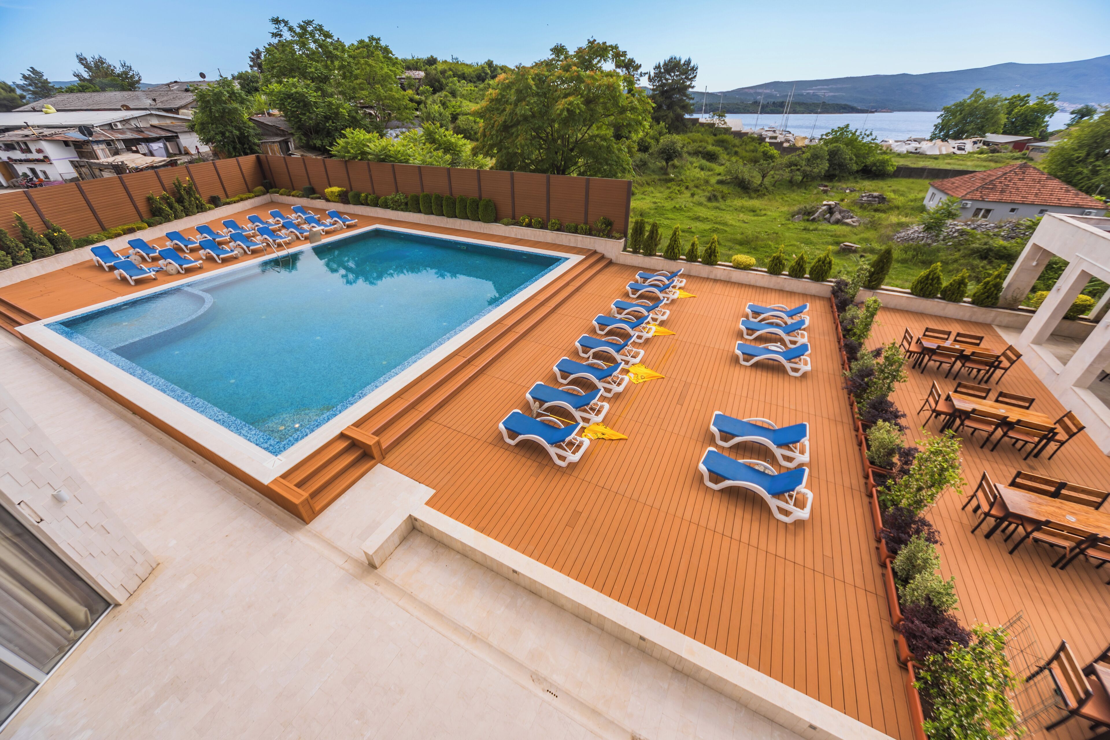 Zona piscina con poltrona relax e terrazza in legno, immersa nel verde e affacciata sull'acqua.