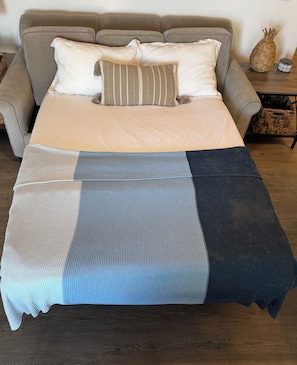 Een bed met een gestreept dekbed, een bank met kussens, en een rieten mandje op een houten tafel.