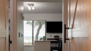 A hallway leading to a kitchen area with a dining table and chairs, a TV mounted on the wall, and a window with blinds. - Romantic Waterfront Getaway
 1st Floor Deep Water Views (Beaufort)