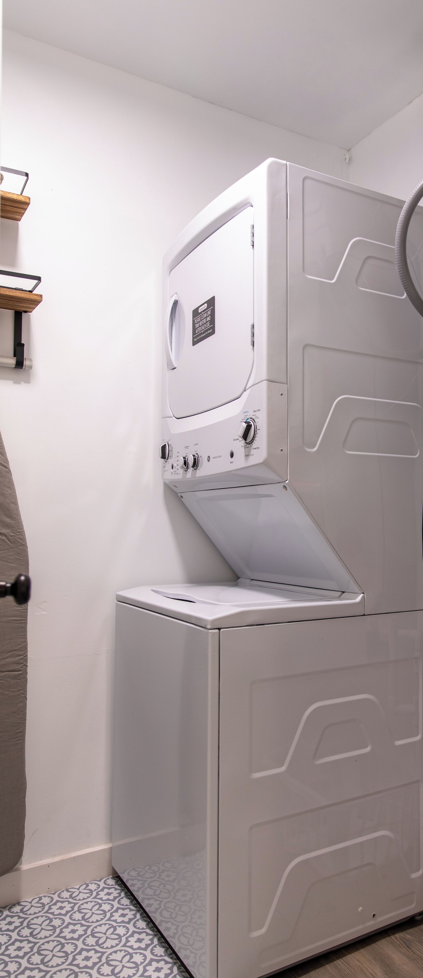 Une petite buanderie moderne et fonctionnelle, dotée d’un lave-linge et d’un sèche-linge intégrés, d’une petite étagère et d’un tapis à motifs.