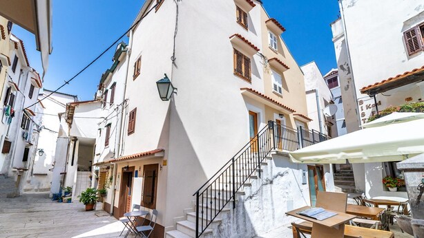A narrow street with white buildings, a staircase, outdoor seating, and a café. - Almost directly on the beach in the old town with many alleyways (Baska)