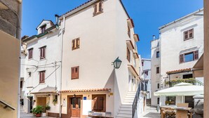 A narrow street with buildings on either side, a staircase leading to a second floor, and outdoor seating with tables and chairs. - Almost directly on the beach in the old town with many alleyways (Baska)